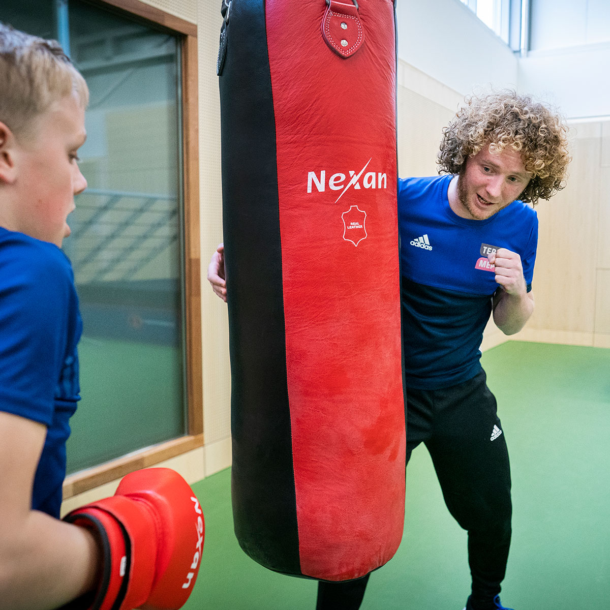 Trainer coacht jongen met bokshandschoenen bij een bokszak